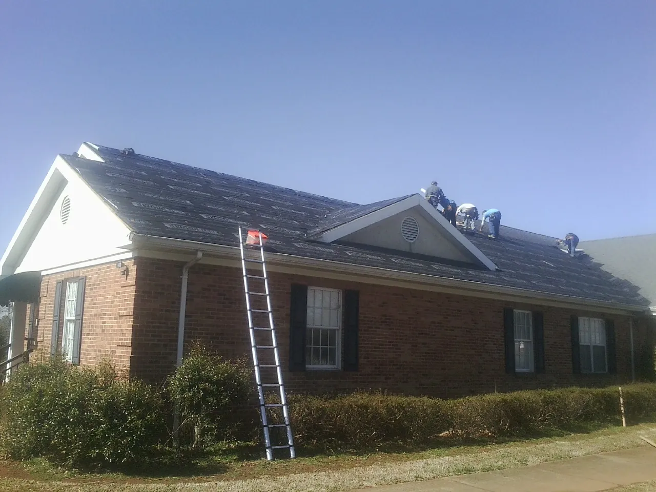Crew tearing shingles off a brick ranch roof with a ladder set — Emergency Roof Repair work by our crew in Hooks