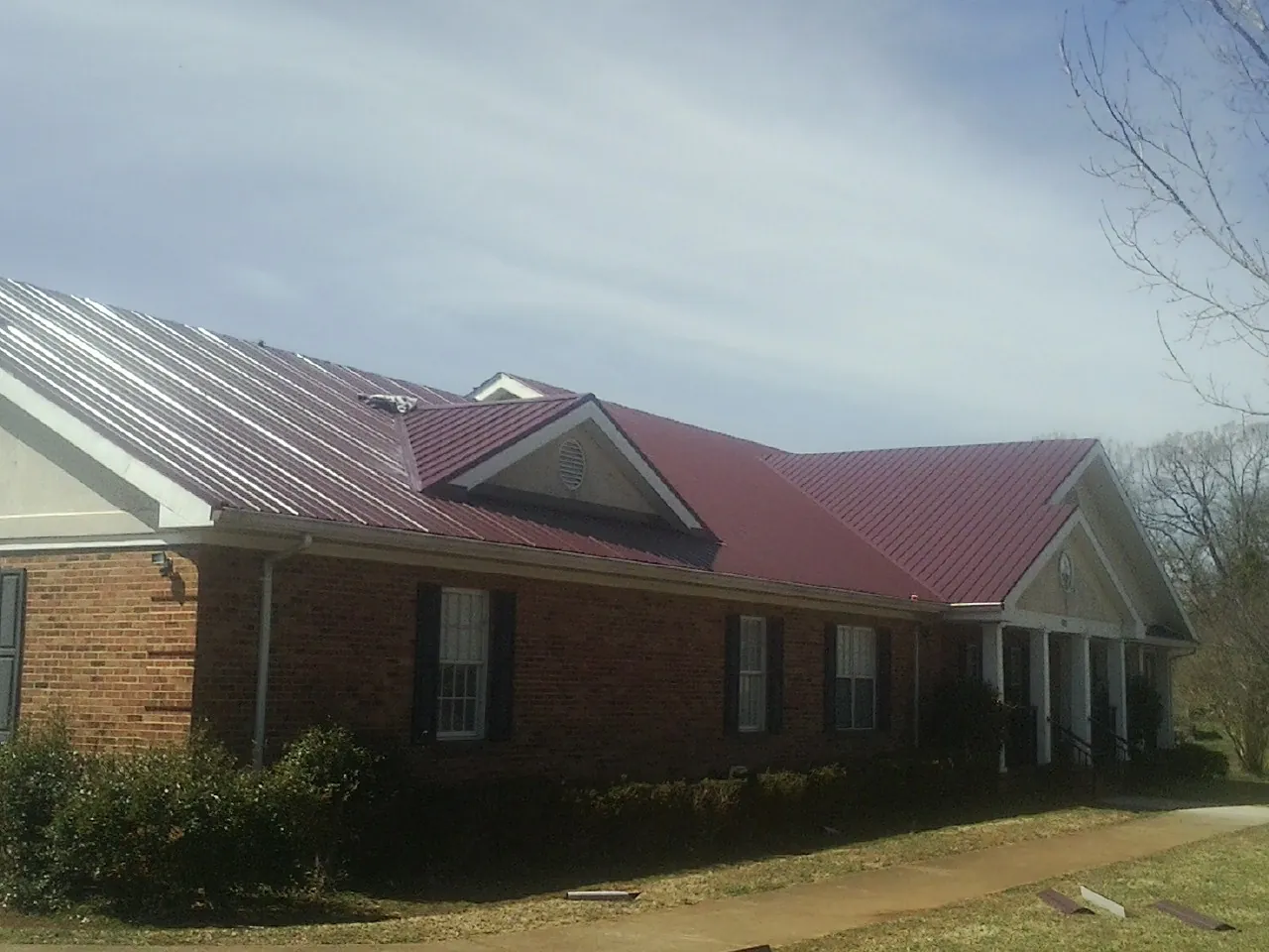 Red metal roof with gabled entries on a long brick building, from a Hail Damage Roof Repair job in Hooks