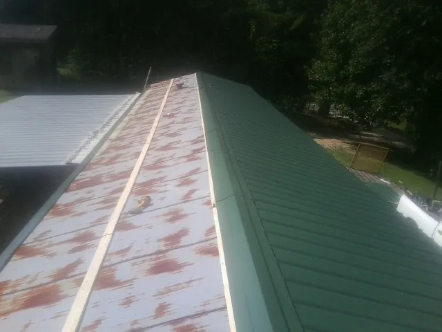 Old rusted panels beside newly installed green metal roofing — Wind Damage Roof Repair by Roofing Brothers in Hooks
