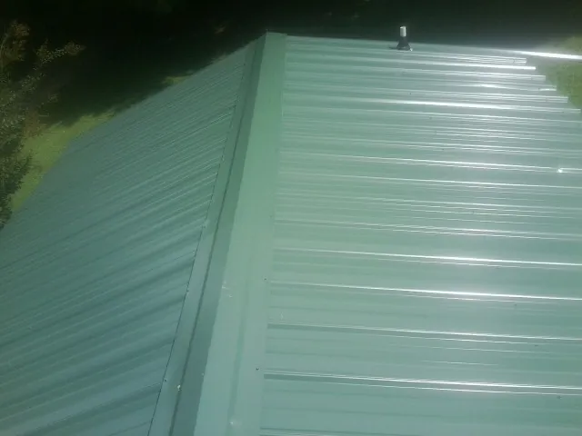 New green metal panels meeting at the ridge of a roof — Flat Roof Repair work by our crew in Hooks